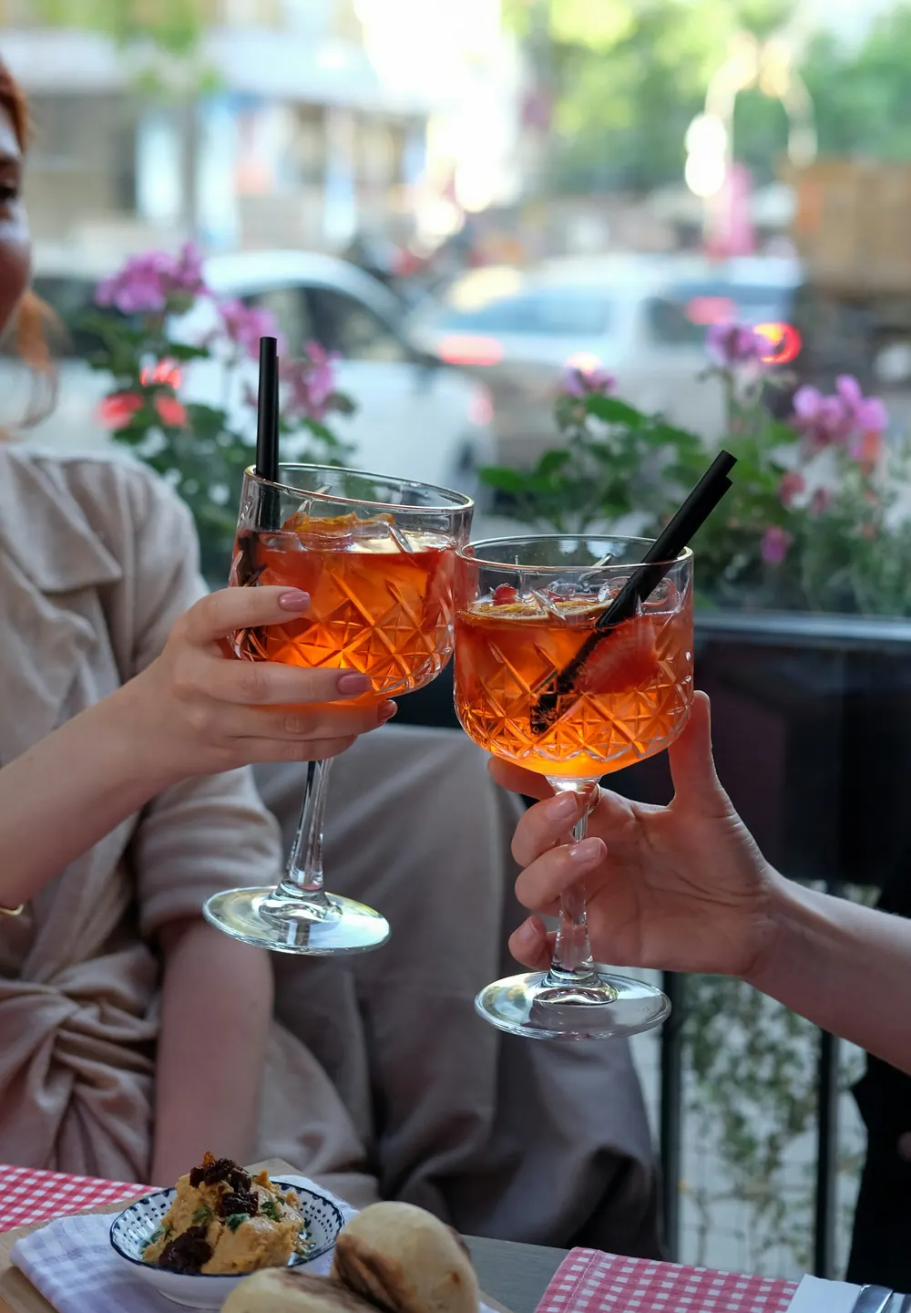 Dos personas brindan con bebidas frías en una terraza con flores