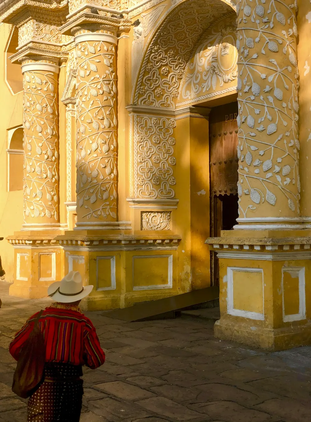 Fachada amarilla con relieves blancos de la Iglesia de La Merced, con un hombre en traje típico al pie