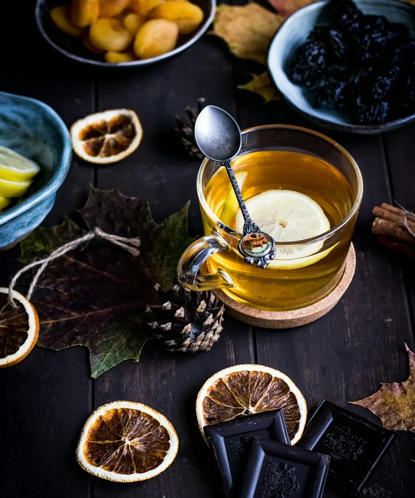 Taza de té de vidrio junto a chocolate oscuro y naranjas deshidratadas