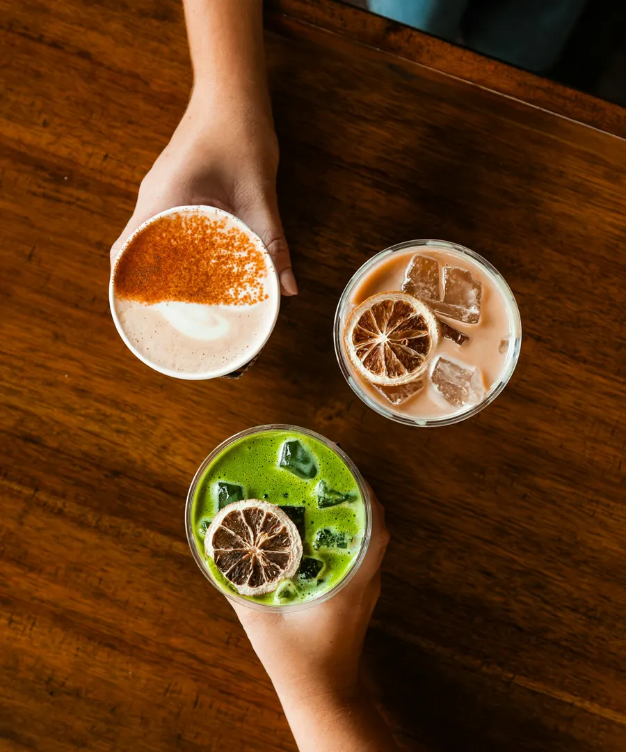 Tres bebidas de té, chai, té helado con naranja deshidratada y matcha, sobre una mesa de madera